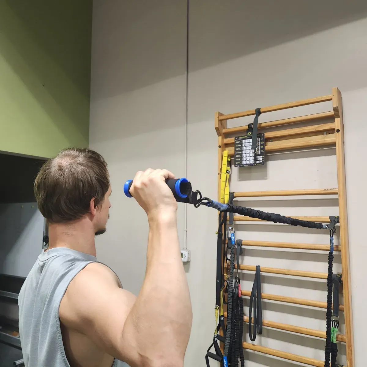 Tube bands with handles, a loop band and suspension straps hanging from wall bars, with a man pulling one tube band by its handle