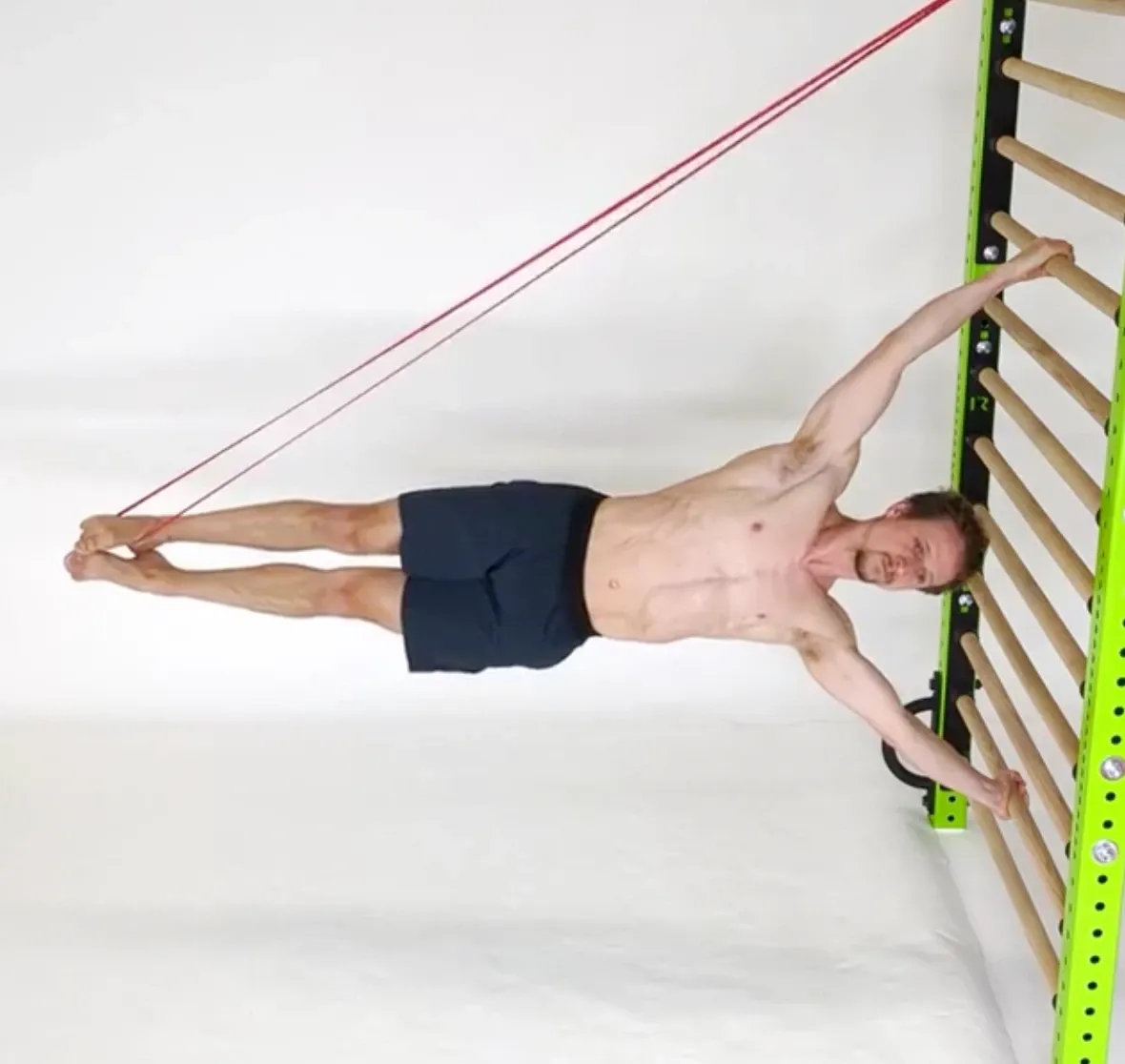 A human flag on wall bars with the feet held up by a resistance band