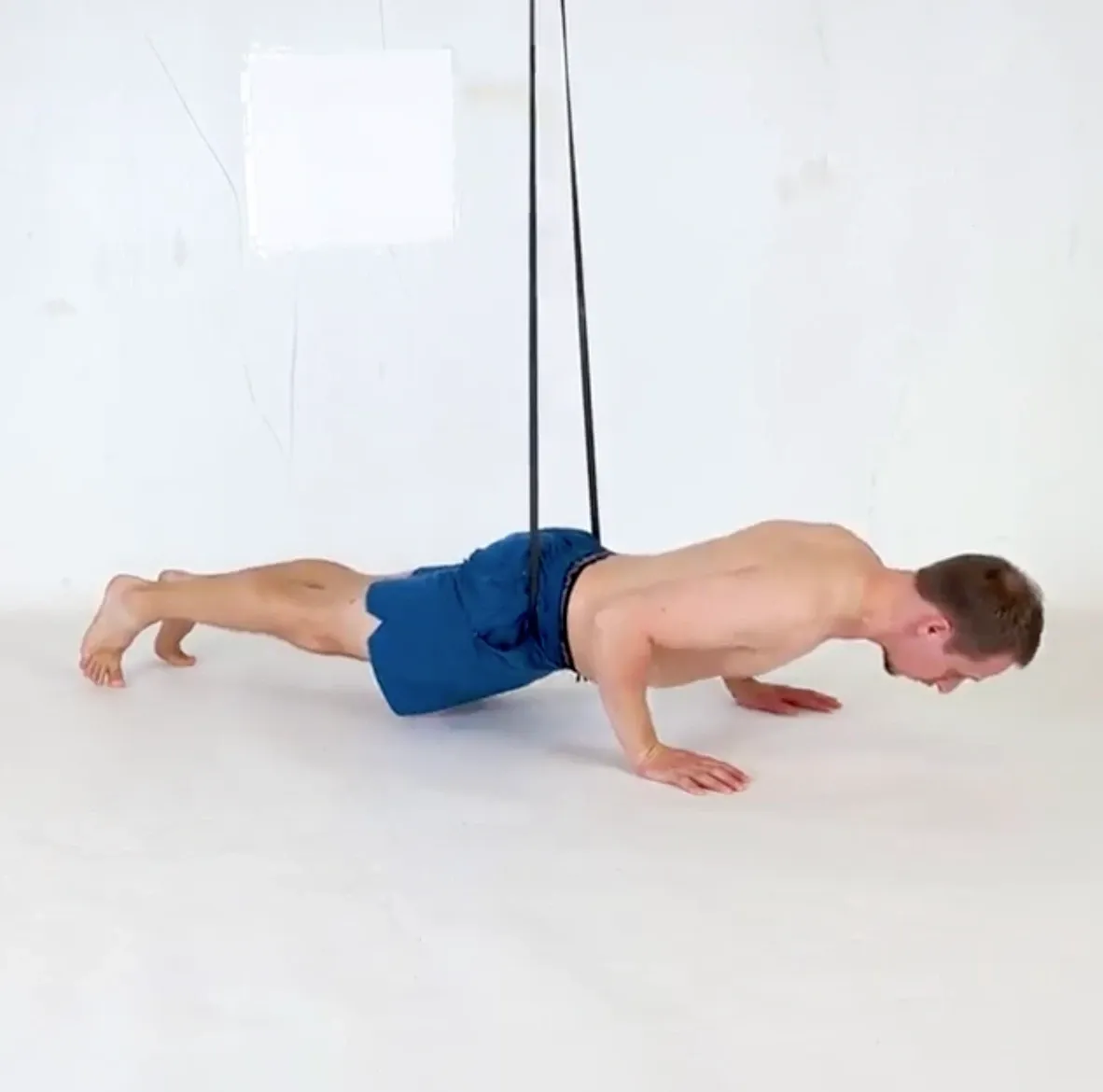 A pushup with a resistance band hanging from above and looped around the hips